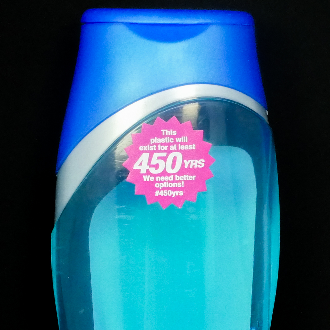 Thumbnail of Close-up photograph of a blue plastic bottle, shaped like a liquid soap container. On the front of the bottle is a magenta, sunburst-shaped sticker that says, 'This plastic will exist for at least 450 YRS. We need better options! #450yrs.'