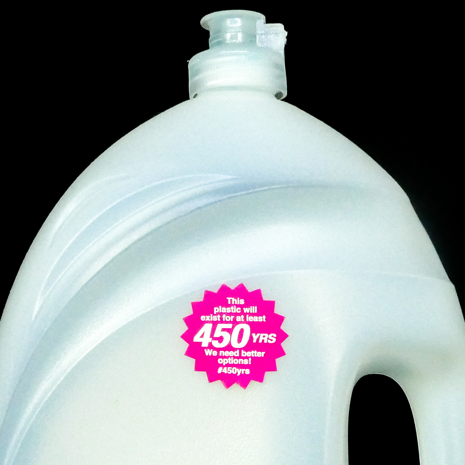 Thumbnail of Close-up photograph of a clear, plastic laundry detergent container. On the front of the container, is a magenta, starburst-shaped sticker that says, 'This plastic will exist for at least 450 YRS. We need better options! #450yrs.'
